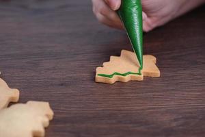 primer plano de dibujo de galletas de azúcar de árbol de Navidad sobre fondo de mesa de madera con glaseado. foto