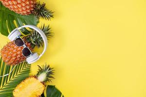 Funny pineapple wearing white headphone, listen music, isolated on yellow background with tropical palm leaves, top view, flat lay design concept. photo