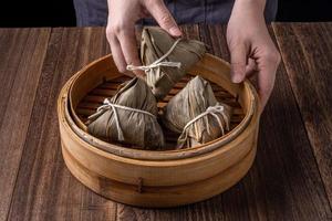 Rice dumpling, zongzi - Dragon Boat Festival, Bunch of Chinese traditional cooked food in steamer on wooden table over black background, close up, copy space photo