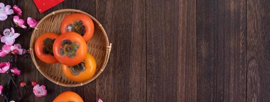 Top view of fresh sweet persimmons with leaves on wooden table background for Chinese lunar new year photo