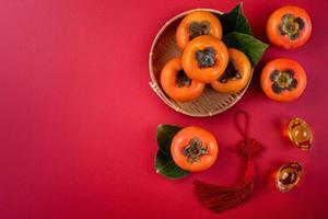 Top view of fresh sweet persimmons with leaves on red table background for Chinese lunar new year photo