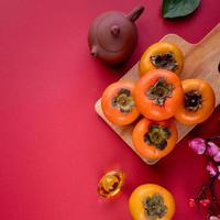 Top view of fresh sweet persimmons with leaves on red table background for Chinese lunar new year photo