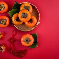 Top view of fresh sweet persimmons with leaves on red table background for Chinese lunar new year photo