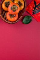 Top view of fresh sweet persimmons with leaves on red table background for Chinese lunar new year photo