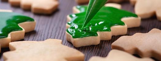 primer plano de dibujo de galletas de azúcar de árbol de Navidad sobre fondo de mesa de madera con glaseado. foto