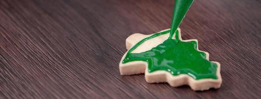 primer plano de dibujo de galletas de azúcar de árbol de Navidad sobre fondo de mesa de madera con glaseado. foto