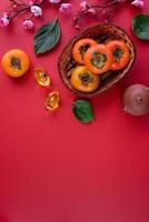 Top view of fresh sweet persimmons with leaves on red table background for Chinese lunar new year photo