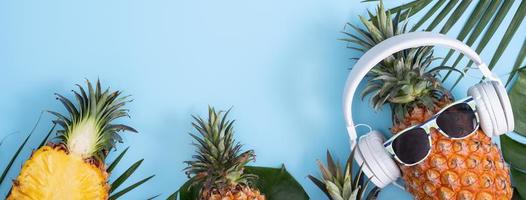 Funny pineapple wearing white headphone, concept of listening music, isolated on colored background with tropical palm leaves, top view, flat lay design. photo