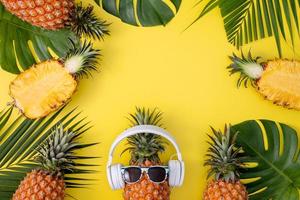 Funny pineapple wearing white headphone, listen music, isolated on yellow background with tropical palm leaves, top view, flat lay design concept. photo