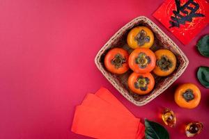 Top view of fresh sweet persimmons with leaves on red table background for Chinese lunar new year photo