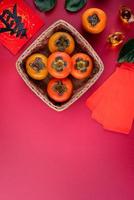Top view of fresh sweet persimmons with leaves on red table background for Chinese lunar new year photo