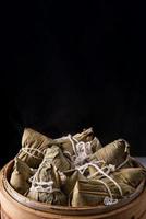 Rice dumpling, zongzi - Dragon Boat Festival, Bunch of Chinese traditional cooked food in steamer on wooden table over black background, close up, copy space photo