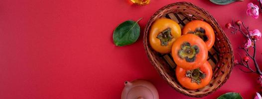 Top view of fresh sweet persimmons with leaves on red table background for Chinese lunar new year photo