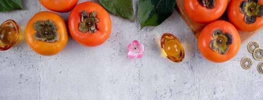 Top view of fresh sweet persimmons with leaves on gray table background for Chinese lunar new year photo