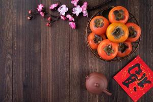 Top view of fresh sweet persimmons with leaves on wooden table background for Chinese lunar new year photo