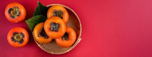 Top view of fresh sweet persimmons with leaves on red table background for Chinese lunar new year photo