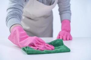 Young woman housekeeper in apron is wearing pink gloves to clean the table, concept of preventing virus infection, housekeeping service, close up. photo