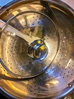 High angle view of a chrome pasta strainer in a pot on a stove. photo