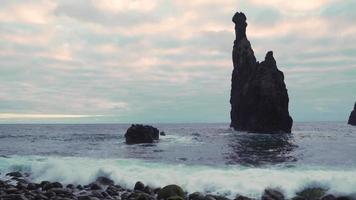 Large rock formations in the sea as waves crash on a stony shore video