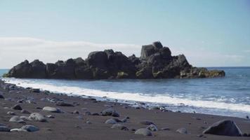 Large rock formations in the sea as waves crash on a stony shore video