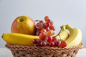 Ripe fruits in wicker basket on gray background. Harvest concept. Bananas, apples and grapes. photo