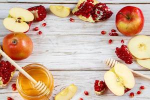 manzanas, granadas y miel sobre fondo blanco de madera. feliz rosh hashaná. símbolos tradicionales de la celebración del año nuevo judío. foto