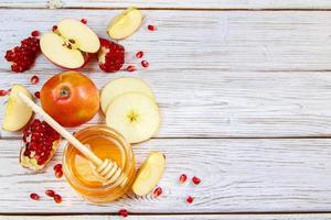 Happy Rosh Hashanah. Traditional symbols of Jewish New Year celebration. Apples, pomegranates and honey on white wooden background. photo