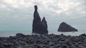 Large rock formations in the sea as waves crash on a stony shore video