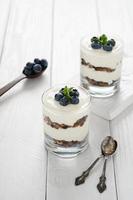 Dessert with cottage cheese, fresh blueberries and granola in a glass on a white wooden background. photo