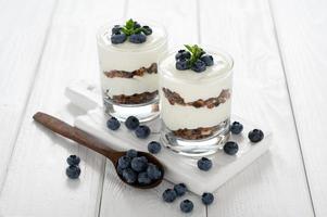Dessert with cottage cheese, fresh blueberries and granola in a glass on a white wooden background. photo