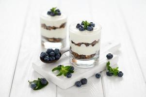 Dessert with cottage cheese, fresh blueberries and granola in a glass on a white wooden background. photo