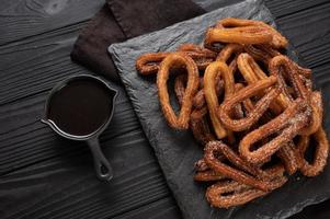 Homemade churros with chocolate on a dark wooden rustic background. photo