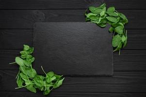 Kitchen table with stone cutting board, decorated with herbs. Presented on the black wooden background with center empty space. Table top view. photo