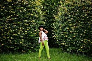Amazing african american model woman in green pants and black hat posed at park. photo
