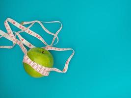 manzana verde con cinta métrica sobre fondo azul. el concepto de seguimiento de la ingesta de pérdida de peso, dieta y nutrición. copie el espacio. foto