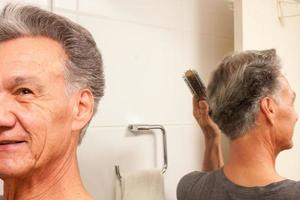 hombre maduro 60plus peinando su cabello mayormente gris en la parte posterior de su cabeza frente a un espejo foto