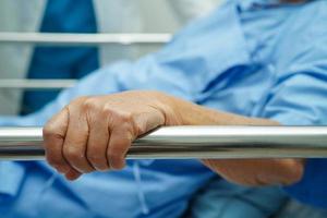 Asian elder senior woman patient holding bed rail while lie down with hope waiting her family in hospital. photo