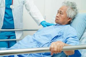 Asian elder senior woman patient holding bed rail while lie down with hope waiting her family in hospital. photo