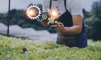 un hombre de negocios futurista cultiva verduras y cultivos usando tecnología moderna de inteligencia artificial usando teléfonos móviles, sensores de temperatura y humedad, rastreo de agua, control climático, íconos de datos holográficos. foto