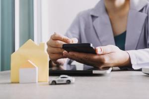 The hand is pressing calculators, piggy bank with wooden house. buy or rent question on note with calculators on desk. Save money and buy house concept. photo