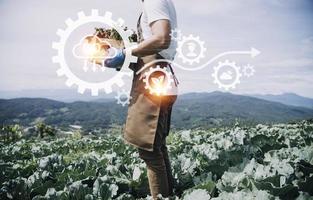 un hombre de negocios futurista cultiva verduras y cultivos usando tecnología moderna de inteligencia artificial usando teléfonos móviles, sensores de temperatura y humedad, rastreo de agua, control climático, íconos de datos holográficos. foto