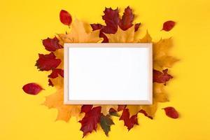 Empty wooden frame mock up and autumn leaves on yellow background. Template for design. photo