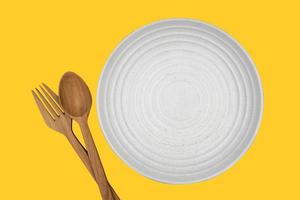 A white round empty plate with fork and spoon on dark background for food and ingredient concept set up. Isolate on yellow background. photo