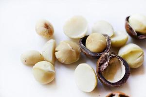 nuez entera y núcleo de macadamia sobre un fondo blanco. deliciosos frutos secos enteros. foto