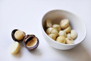 nuez entera y núcleo de macadamia sobre un fondo blanco. deliciosos frutos secos enteros. foto