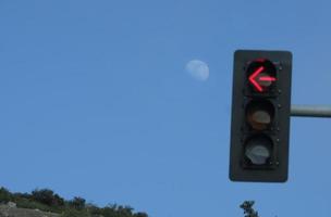 The arrow of a traffic light pointing at the moon with blue sky around it photo