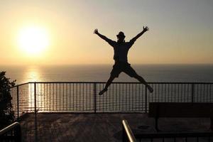 silueta de un hombre saltando cerca de la costa durante la puesta de sol foto