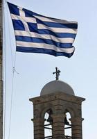 bandera griega ondeando en el viento con una torre de iglesia en el fondo foto