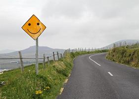 Optimism - Yellow road sign with smiley ahead of a curve in a hilly landscape photo