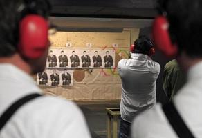 Riga, Latvia - April 15, 2019 - A young man shoots a gun at paper targets at a shooting range seen from behind. photo